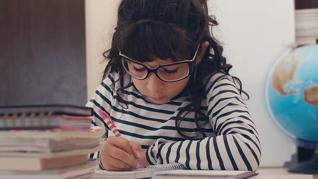 Close up of cute caucasian girl with glasses writing homework at home, 4k