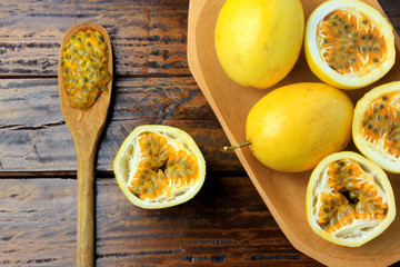yellow passion fruit and passion fruit cut in half in wooden bowl on wooden table.
