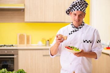 Young professional cook preparing salad at kitchen