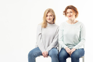 Modern adult woman with teenage girl sitting on chairs on white background. Family concept