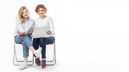 Modern adult woman with teenage girl sitting on chairs sharing laptop on white background