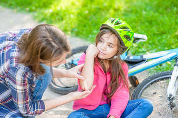 Young mother puts a bandage on a wound to little girl, who fell off his bicycle