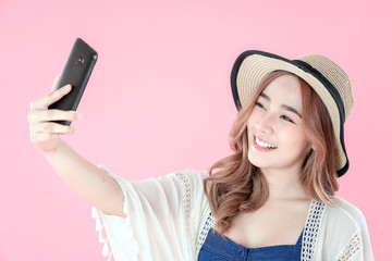 Naklejka premium Asian woman take selfie by smartphone to post on social media, summer holiday clothing, pink background