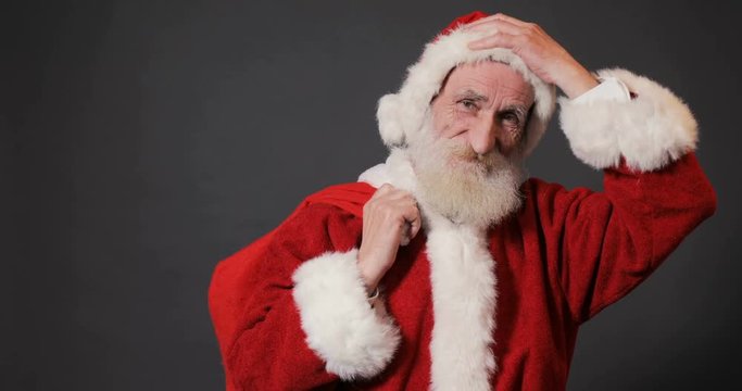 Old, kind santa with long white beard showing red bag full of chistmas gifts, isolated shoot in gray background