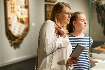 Girl with woman looking with interest at art objects in museum