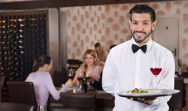 Waiter holding tray at restaurant with customers