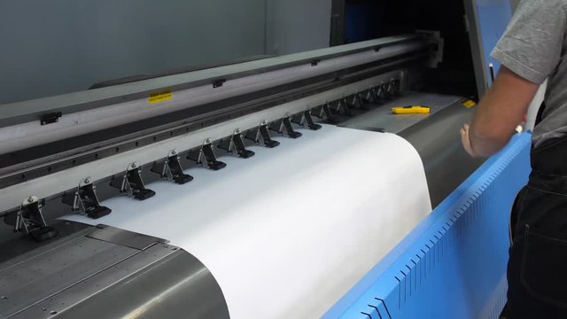 Preparation for the large-format inkjet printing press. The male hands of the worker insert clean printing paper into the printer. 4k