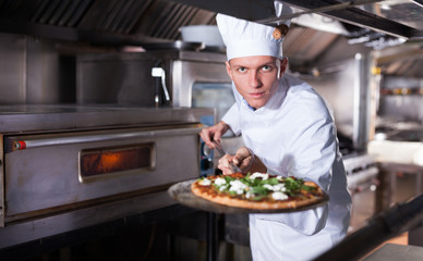 Young chef holding shovel with cooked pizza