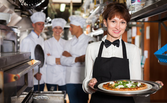 Smiling waitress with pizza in restaurant kitchen