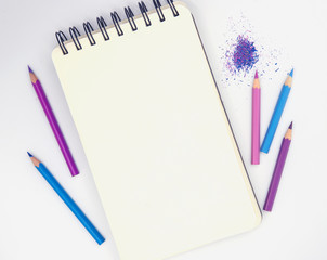 Vertical sketchbook and pink violet pencils on white background. Artistic table top view photo.