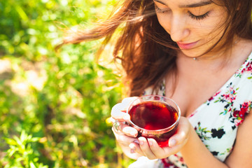 Young beautiful girl with long eye lashes with glass cup of black tea, happy teen girl smiling in...