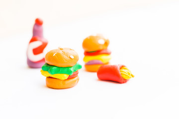 Miniature play dough burgers, hot dog, french fries, chicken thigh on white isolated background, unhealthy fast food school meal concept, artificial or plastic modern colorful dyed food, copy space  