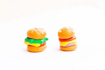 Miniature play dough burgers, hot dog, french fries, chicken thigh on white isolated background, unhealthy fast food school meal concept, artificial or plastic modern colorful dyed food, copy space  