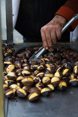 Fresh hot roasted chestnuts sold at the street, roasting process on hot pan, male hand turning the ready chestnuts, nut shells, traditional eastern turkish delicious snack in Istanbul, copy space