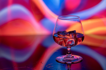 Glass of brandy with ice on a colored background