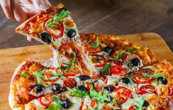 woman Hand takes a slice of Pizza Margherita or Margarita with Mozzarella cheese, tomato, olive. Italian pizza on wooden table background