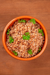 Buckwheat in a rustic earthenware bowl, garnished with fresh parsley leaves, shot from above on a dark wooden background with a place for text