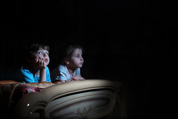 Fototapeta na wymiar Small children in a dark room watching TV