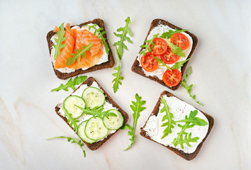 Smorrebrod - traditional Danish sandwiches. Black rye bread with salmon, cream cheese, cucumber, tomatoes on wooden background