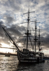 Fototapeta na wymiar Old sailing ship at the city pier on a background of gray sky