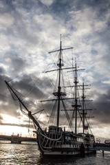 Old sailing ship at the city pier on a background of gray sky