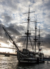 Old sailing ship at the city pier on a background of gray sky