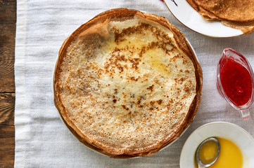 Stack of russian pancakes with butter and strawberry jam on a table