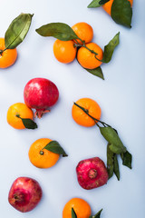 Fresh clementines with leaves and pomegranates scattered on blue background, top view