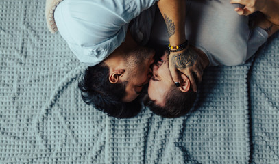 A homosexual couple relaxing in bed hugging and kissing each other. Happy moments of the day.