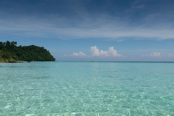 Fototapeta na wymiar Emerald water, blue sky, white clouds and a boat.