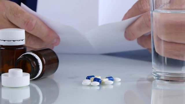 Suffering Man Reading and Checking a Medical Prescript with Pills on the Table