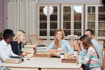 Young casual multiethnic people, muslim Arabian and African guys and caucasian girls, students preparing for exams, reading big thick books and sharing opinions. Co-working and education concept