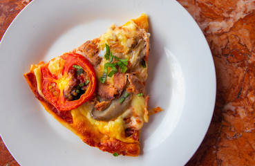Piece of pizza with tomato, herbs and cheese on white plate. Pizza slice on stone table top view. Yummy fresh pizza