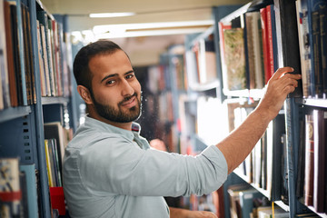 Adult Arabian bookseller picking out a book for customer standing between shelves in the bookshop