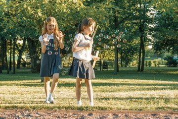 Two little girl friends schoolgirl 7, 8 years old play with soap bubbles on the meadow in the park.