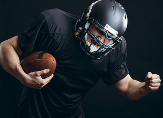 American football sportsman player in black outfit and helmet runing, isolated on black background