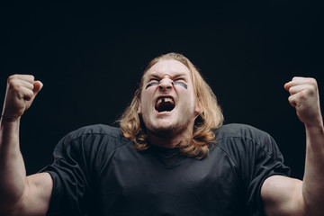 Isolated studio shot of overwhelmed fair-haired football player with a broken tooth celebrates...