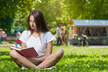 Obraz premium Brunette Student Girl Sitting on Green Grass in Park
