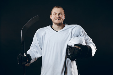Obraz premium Portrait of cheerful handsome hockey player getting into the mood for winning before game starts. Sportsman in white uniform smiling at camera isolated on black