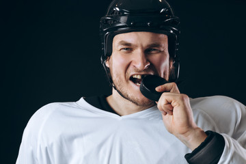 Caucasian Hockey player tastes the puck, having fun, demonstrates the way he lost the tooth, looking at camera isolated on black background.