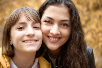 Portrait of pretty woman and teen girl. They are posing in autumn park. Beautiful landscape at fall season.