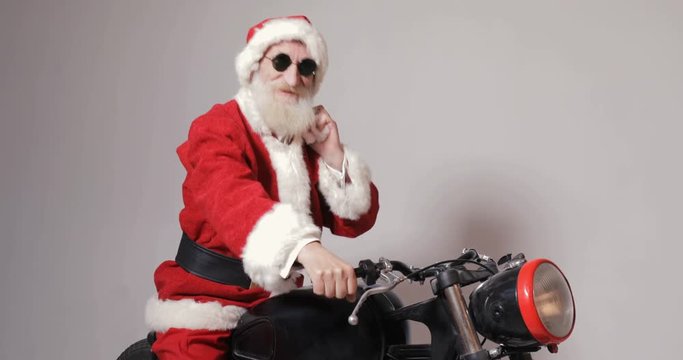 Modern santa delivering presents by cool black and red motorcycle, holding big bag with gifts on the shoulder as sitting on vehicle, isolated indoor