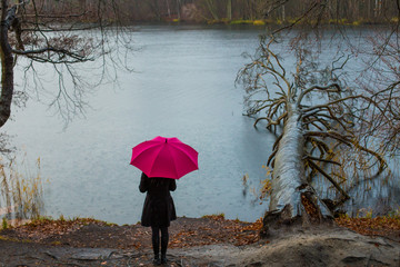 A woman stands alone in cloudy rainy weather by a lake