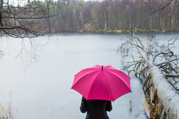 A woman stands alone in cloudy rainy weather by a lake