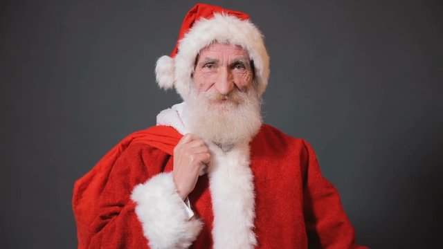 Santa Claus standing with big red bag full of chistmas gifts, portrait shoot in gray background