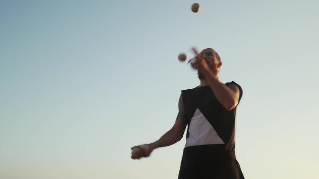 Handsome tattooed man juggling balls against the blue sky shaky footage