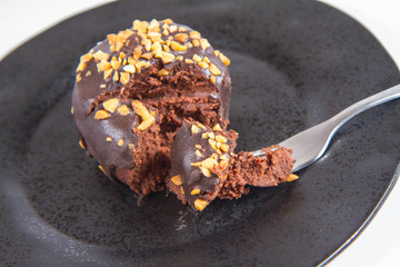 Rum ball decorated with chocolate and nuts on a black plate eaten with a fork on a white background