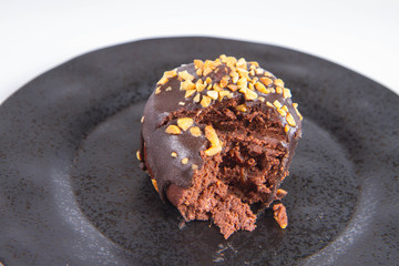 Rum ball decorated with chocolate and nuts on a black plate, partially eaten, on a white background