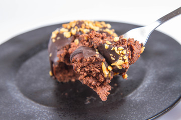 Rum ball decorated with chocolate and nuts on a black plate eaten with a fork on a white background