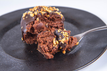 Rum ball decorated with chocolate and nuts on a black plate eaten with a fork on a white background